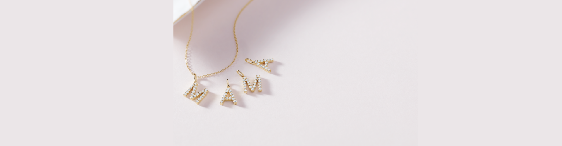 Four yellow gold and diamond initial pendants spelling MAMA, spread out underneath a yellow gold chain.